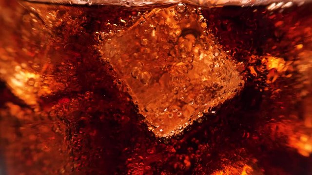 Macro shot of glass with cola and ice cubes. A lot of bubbles going up. 4k.