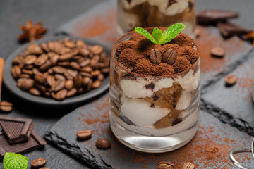 Classic tiramisu dessert in a glass on stone serving board on dark concrete background