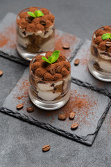 Classic tiramisu dessert in a glass on stone serving board on dark concrete background