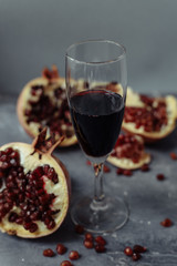 A wine glass with red wine stands on a gray grunge background next to grenades. Fruits and pomegranate wine