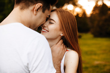 Side view portrait of a lovely couple having fun laughing while embracing with closed eyes outside against the sunset while traveling in their vacation time.