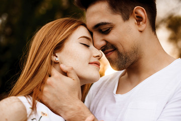Fototapeta premium Close up portrait of a lovely young couple embracing before kissing smiling against sunset while dating in their vacation time.