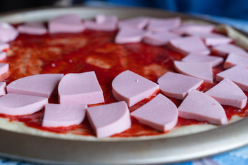 pizza dough smeared with ketchup and with slices of sausage as background