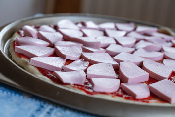 pizza dough smeared with ketchup and with slices of sausage as background