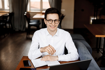 Portrait of a handsome caucasian businessman sitting at his desk smiling while wearing eyeglasses dressed in white.