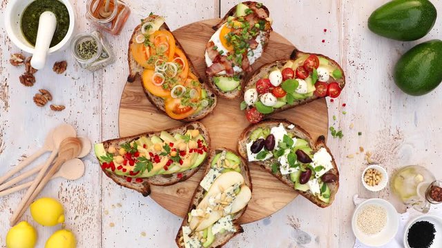 Assorted open faced sandwiches, Open avocado sandwiches made of slices of sourdough bread with various toppings on a round board, on a white wooden table, top view, 4k.