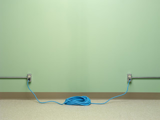 Dangerous electrical wiring with blue coiled extension cord plugged into two AC wall outlets on...