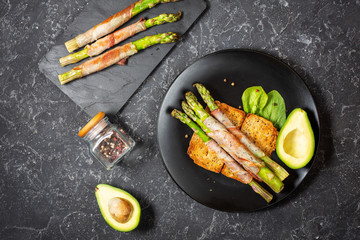 Grilled green asparagus wrapped with bacon and avocado on toasts