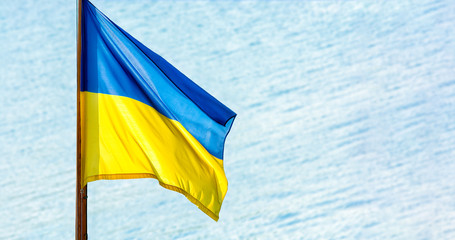 Ukrainian flag against a blue sea waves. Yellow and blue colors. National symbol of Ukraine.