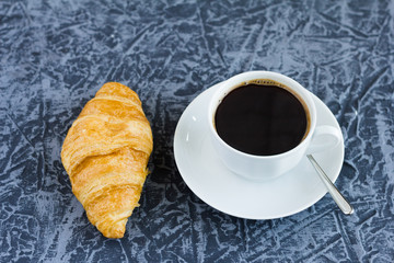 a Cup of black coffee and a croissant on the table
