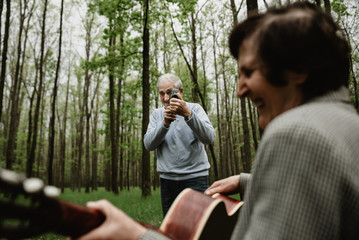 Obraz premium Loving mature couple coming on picnic with guitar. Happy senior couple playing a guitar and having a romantic date outdoor. senior people spending time together on spring field. Man with old camera.