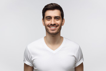 Portrait of smiling man in white t-shirt looking at camera, isolated on gray background