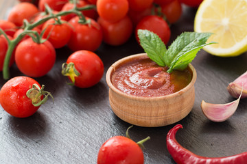 freshly prepared ketchup in a wooden bowl near cherry tomatoes, chilli peppers, lemon, garlic