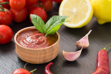 freshly prepared ketchup in a wooden bowl near cherry tomatoes, chilli peppers, lemon, garlic