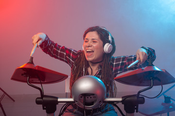 Emotions, music, hobbies and people concept - young woman playing the electronic drum set in studio