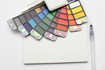 Watercolor paint rainbow palette with brush on white texture paper. Flat lay.