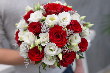 Classic emotional wedding bouquet of white and red roses in the hands of a young guy