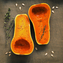 Halves of raw pumpkin or butternut squash with herbs for cooking on parchment paper. Top view, flat lay.