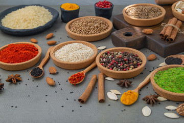 Spices lie in bowls and wooden spoons on a gray background , top view, soft focus. Spices and seasonings for cooking in the composition on the table.