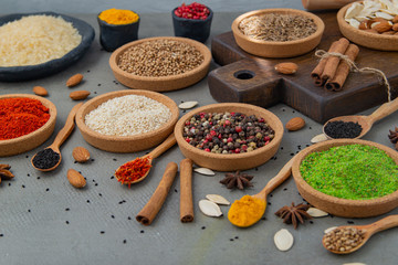 Spices lie in bowls and wooden spoons on a gray background , top view, soft focus. Spices and seasonings for cooking in the composition on the table.