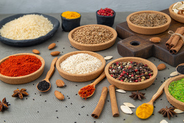 Spices lie in bowls and wooden spoons on a gray background , top view, soft focus. Spices and seasonings for cooking in the composition on the table.