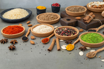 Spices lie in bowls and wooden spoons on a gray background , top view, soft focus. Spices and seasonings for cooking in the composition on the table.