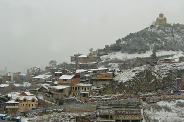 View of Tbilisi Old town Sololaki in winter while snow. Orange snowy roofs, orthodox church, river Kura make atmosphere of the city. Georgia Country.