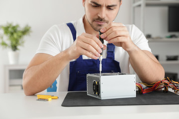 Male technician repairing power supply unit at table indoors