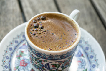 Cup of coffee with foam on a wooden table close-up. Traditional black Turkish coffee in a beautiful Cup with national patterns.