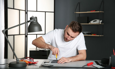 Technician repairing mobile phone at table in workshop