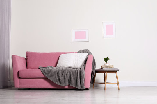 Cozy living room interior with sofa, pillow and plaid near light wall. Space for text