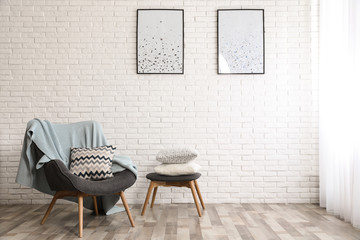 Stylish interior with plaid, pillows and armchair near brick wall, space for text