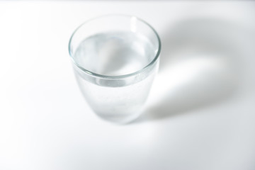 Top view of round glass filled with cold mineral water on bright, blank surface. Reflection of the glass visible on the surface. High exposure photo. Side white light