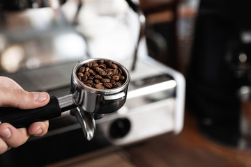 Barista holding portafilter with coffee beans near machine, closeup. Space for text