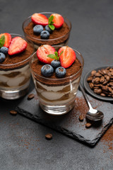 Classic tiramisu dessert with blueberries and strawberries in a glass on stone serving board on dark concrete background