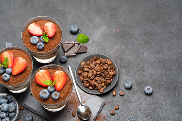 Classic tiramisu dessert with blueberries and strawberries in a glass on stone serving board on dark concrete background