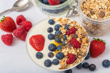 White yogurt in bowl with oatmeal and strawberries, blueberries and raspberries on the top on white background.