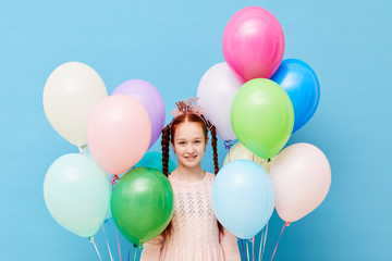 Fototapeta na wymiar Waist up portrait of cute red-haired girl holding balloons standing against pastel blue background, Birthday party concept, copy space