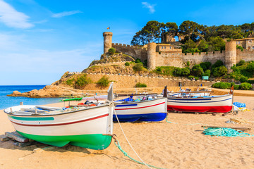 Fishing boats on golden sand beach in bay with castle in background, Tossa de Mar, Costa Brava,...