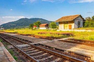 Fototapeta na wymiar Railroad tracks and old wooden building at the abandoned railway station Cornet at Tutulesti, Romania, Valcea County