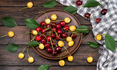 Red and yellow sweet sweet cherries in a plate on a wooden background. view from above