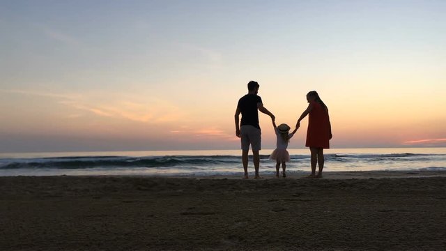 Happy parents swinging child on the beach.