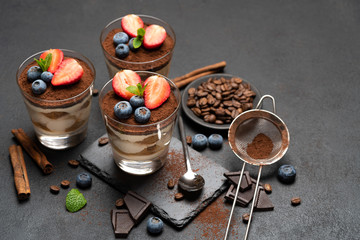 Classic tiramisu dessert with blueberries and strawberries in a glass on stone serving board on dark concrete background