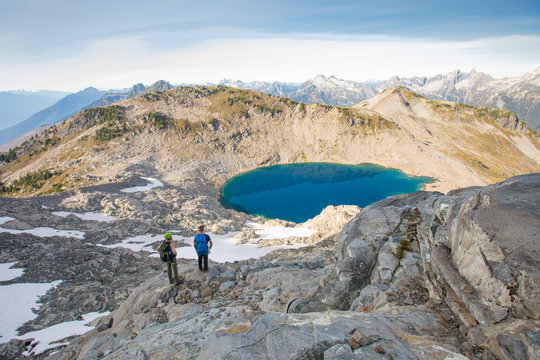 Mountaineers look down on alpine tarn and surrounding peaks.