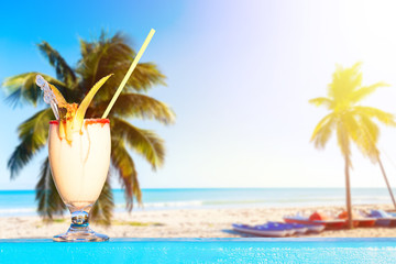 Refreshing pina colada cocktail against amazing beach background with palms and ocean. Summer...