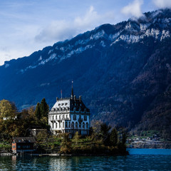 View across Brienzersee Lake, Switzerland with the white facade of Iseltwald castle reflected in the calm waters of the lake and Niesen mountain rising up in the far distance
