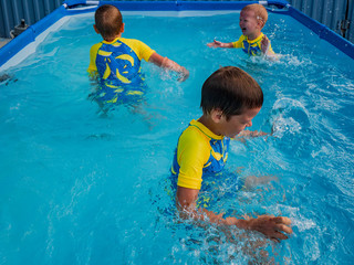 Three happy kids playing in carcas pool in swimwear for boys. Brothers are happy together in warm water on sunny summer day. Concept of learning games for preschoolers.