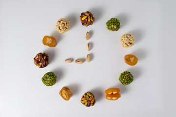 Healthy vegan snack clock. Sugar-free. Dry peach balls with pistachio and peanut cover. Candy sausage. Dried apricots stuffed with almonds. Isolated. Nine o'clock. Morning meal.