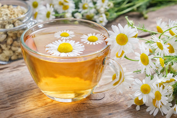 Daisy flowers in transparent glass tea cup, healthy chamomile herbs and glass jar of dry daisies...