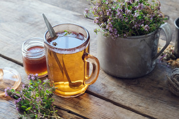 Mug of thyme healthy herbal tea, honey jar and rustic metal cup full of thymus serpyllum medicinal herbs. - obrazy, fototapety, plakaty